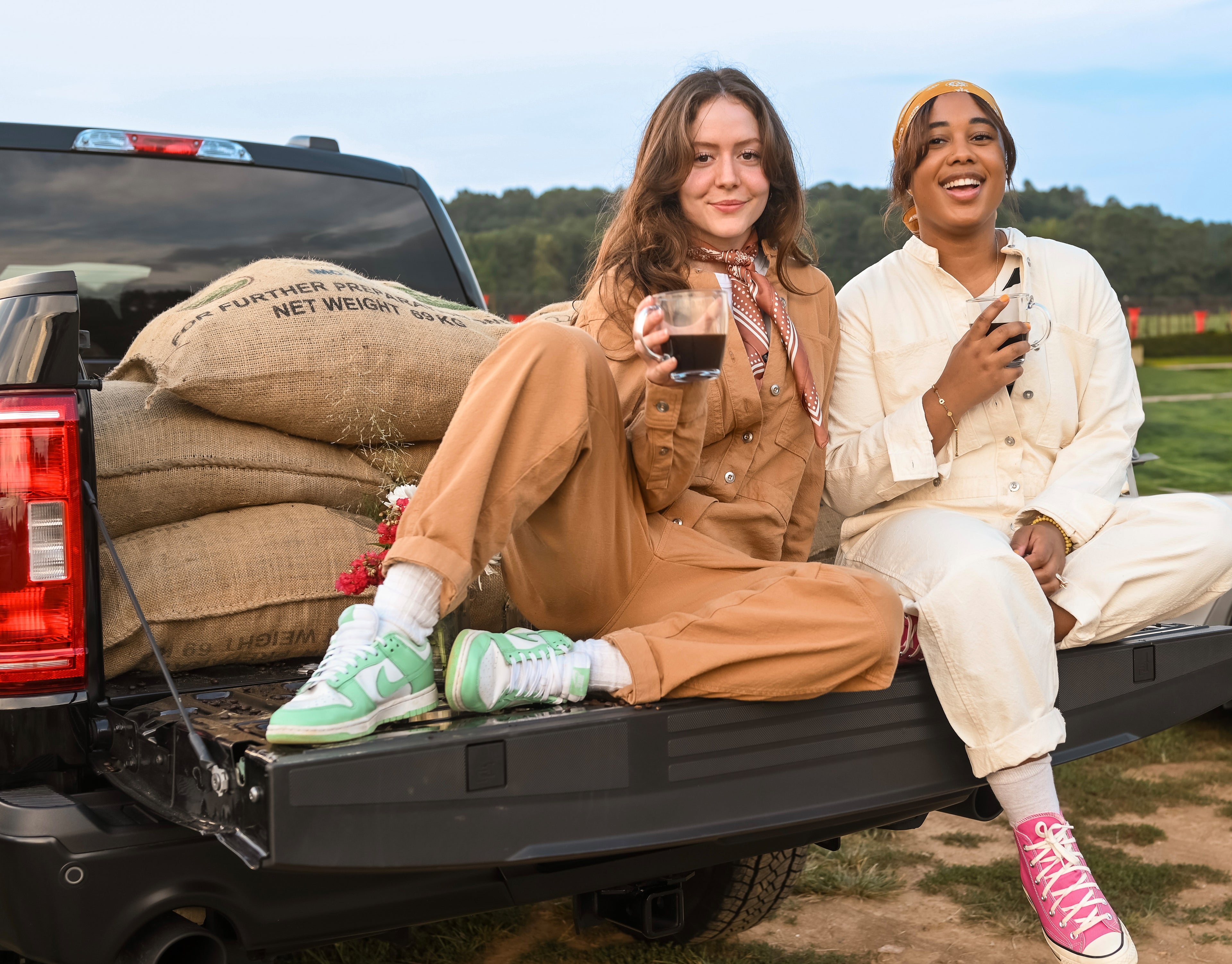 Owners Debra and Isabelle seating in the back of a pick up truck, posing with sacks of beans while holding a cup of coffee